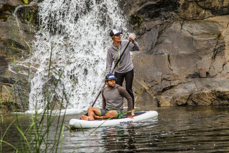 Two People on a Paddleboard Near a Waterfall