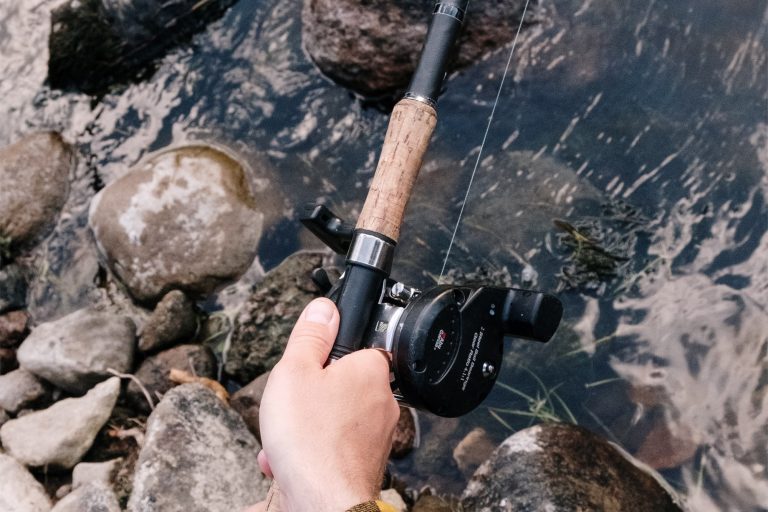 Man Sitting at a Riverbank Holding a Rod